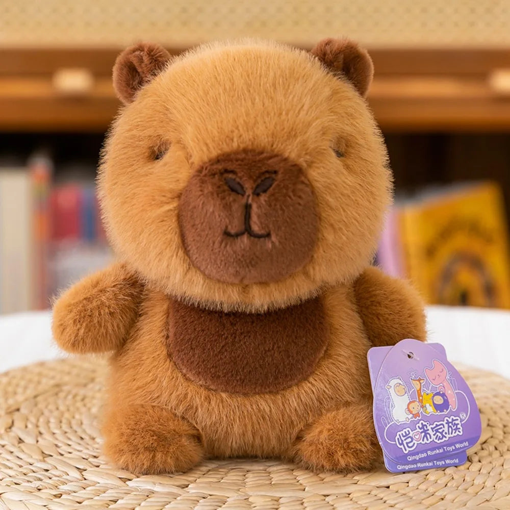 Cute Fun Small Brown Capibara plush toy with a purple tag on a woven surface.