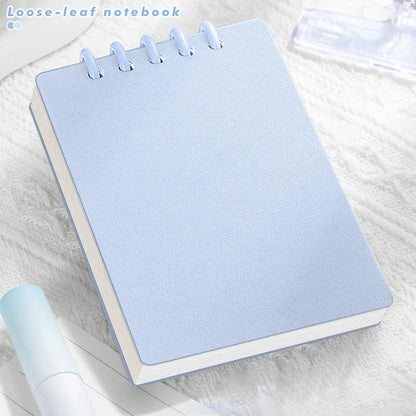 Cute Small notepad with light Pastel blue cover and lined pages on a light wooden surface with magazines underneath.