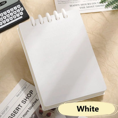 Cute Small notepad with white cover and lined pages on a light wooden surface with magazines underneath.