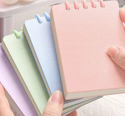 Set of small Cute notebooks in pastel colors held by hands with text indicating thickness and number of pages.
